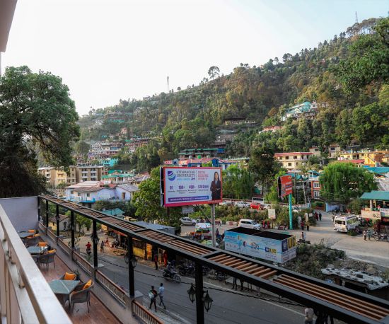 alt-text A balcony with views of an open rooftop dining area and a small town nestled amidst mountains - Vinsober Monal, Nainital