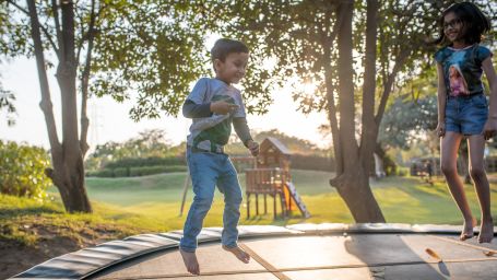 children jumping on a trampoline with trees and the sun set in the background - Karma Lakelands