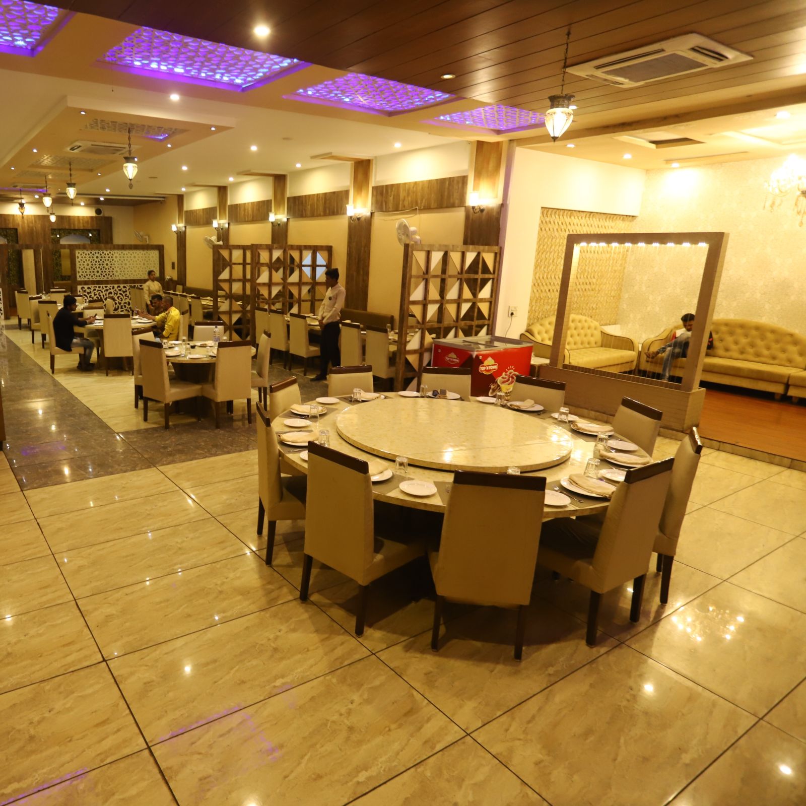 interior of Meadha restaurant at Hotel Manaal By M Square, Pithampur featuring round tables and chairs placed around it