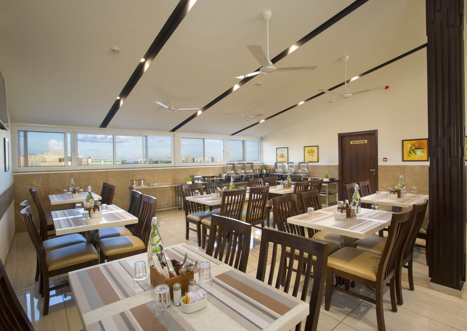 A hotel restaurant with wooden tables and chairs, large windows and ceiling fans - De Venetian by TGI, Brookefield