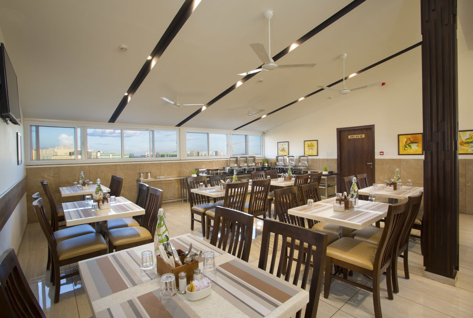 A hotel restaurant with wooden tables and chairs, large windows and ceiling fans - De Venetian by TGI, Brookefield