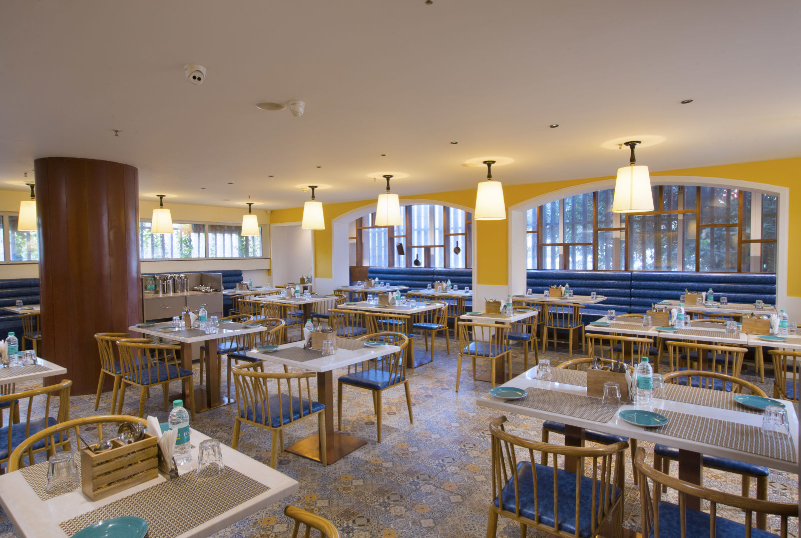 A bright and inviting restaurant interior with yellow walls, pendant lights and blue booth seating - Hotel Southend By TGI - Bommasandra, Bangalore