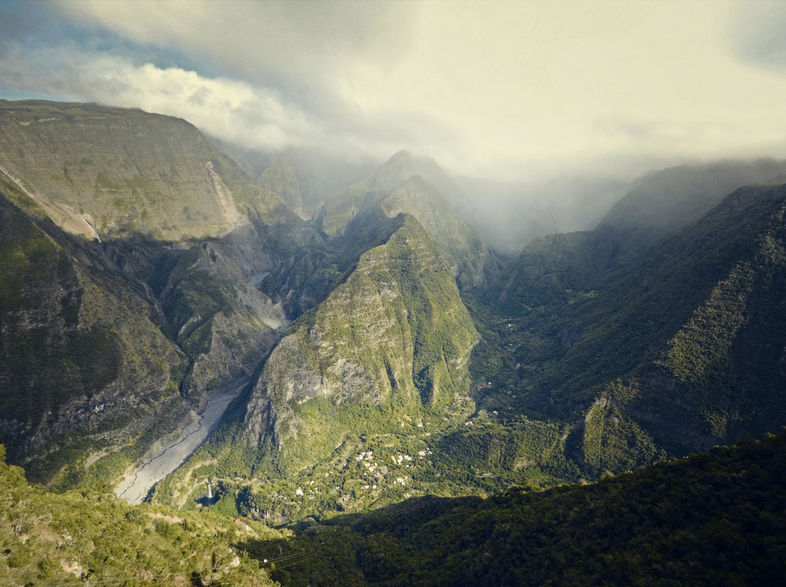 Aerial view of a lush green mountainous landscape shrouded in mist with a winding river in a deep valley.