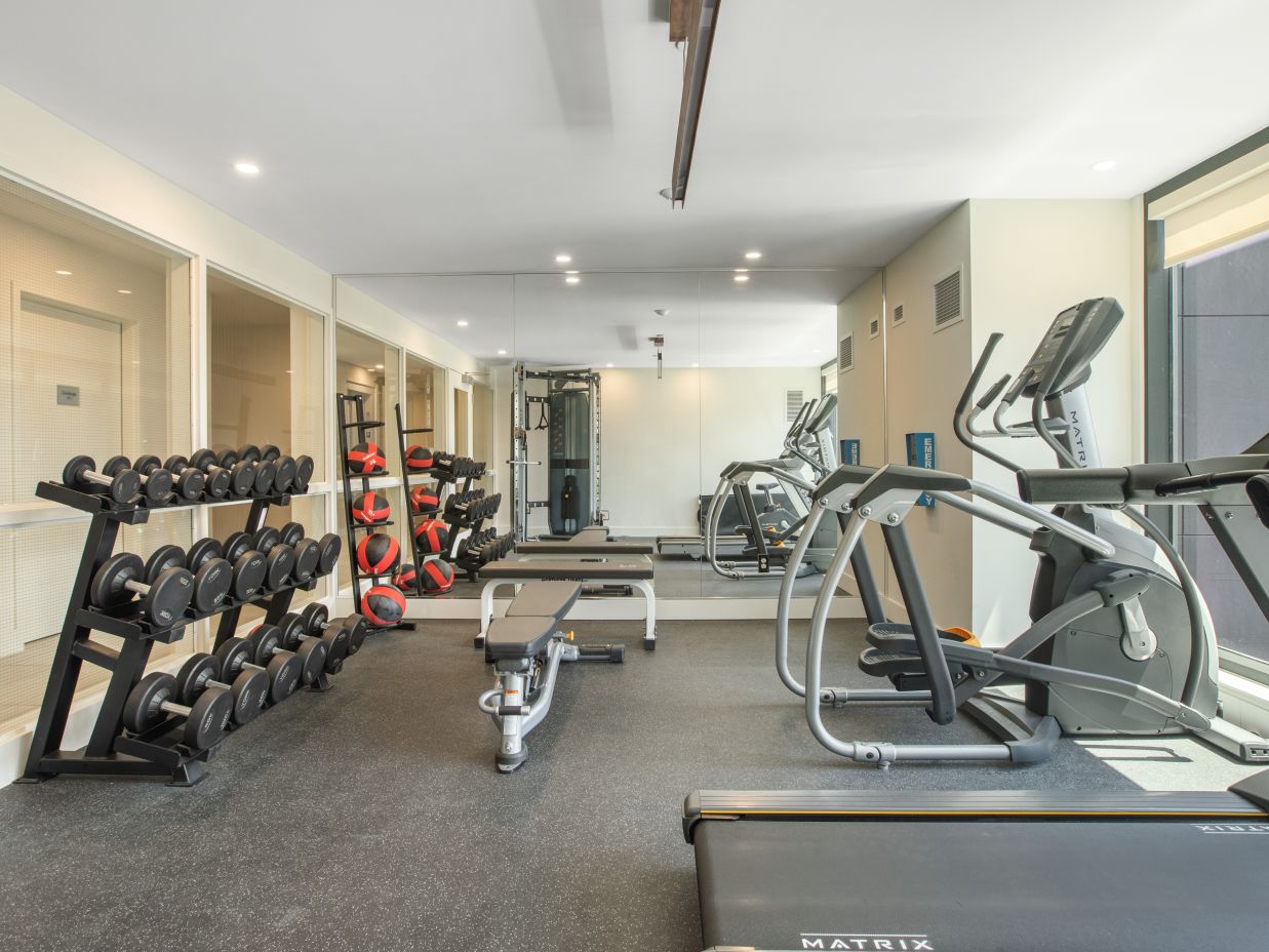 A gym room with equipment to work out including dumbbells and tradmill