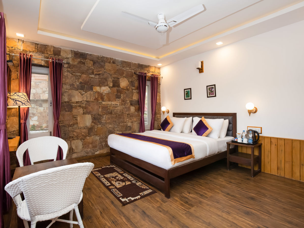 A room with wooden wooden bed, wall paintings, a coffee table and 2 sofa chairs - The Nature's Green Resort, Bhimtal