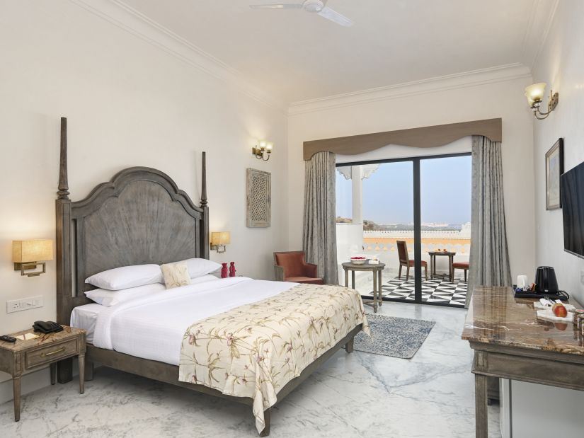 Fateh Vilas Udaipur - Interior view of the Renaissance Room with sit out featuring a king size bed white decor and a balcony