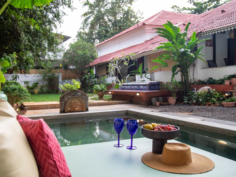 L shaped pool side with two blue wine glasses and surrounded by greenery @ Lamrin Ucassaim Hotel, Goa