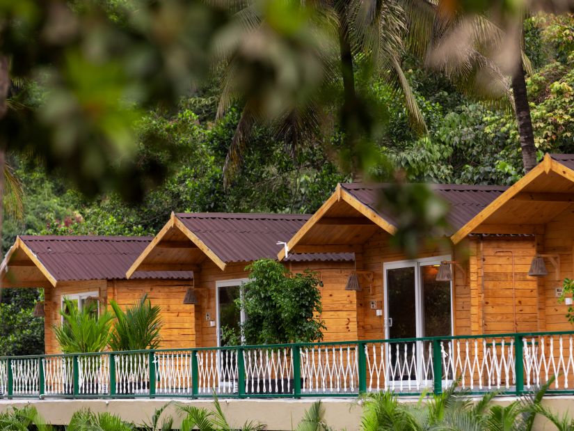 Row of cottages with a railing in front of them and nature in the background - Stone Wood Jungle Resort, Dandeli
