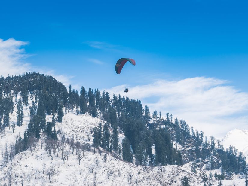 A person paragliding amidst the snow capped mountains