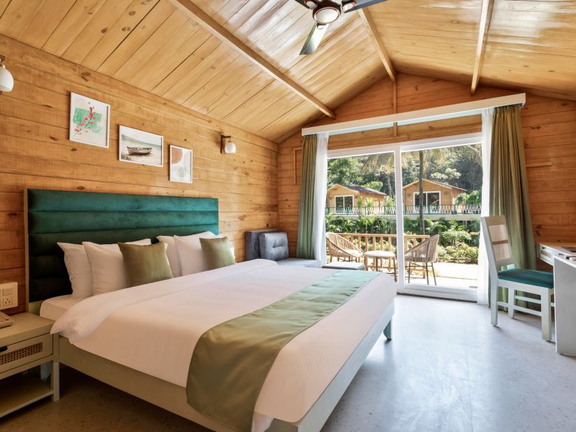 a double bed with pillows on it and entrance to the balcony in view inside one of the rooms - Stone Wood Jungle Resort, Dandeli