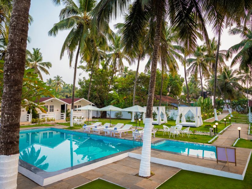 corner view of a swimming pool at a resort in front of cottages surrounded by green trees shot during the day - Stone Wood Hotels & Resorts