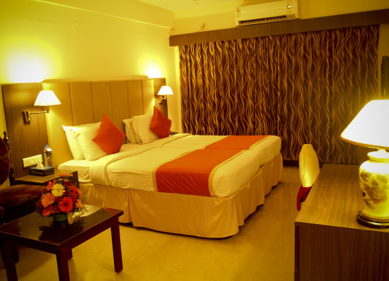 alt-text Hotel Yasodha Towers - Interior view of a bedroom containing a queen size bed illuminated with yellow coloured lamps 