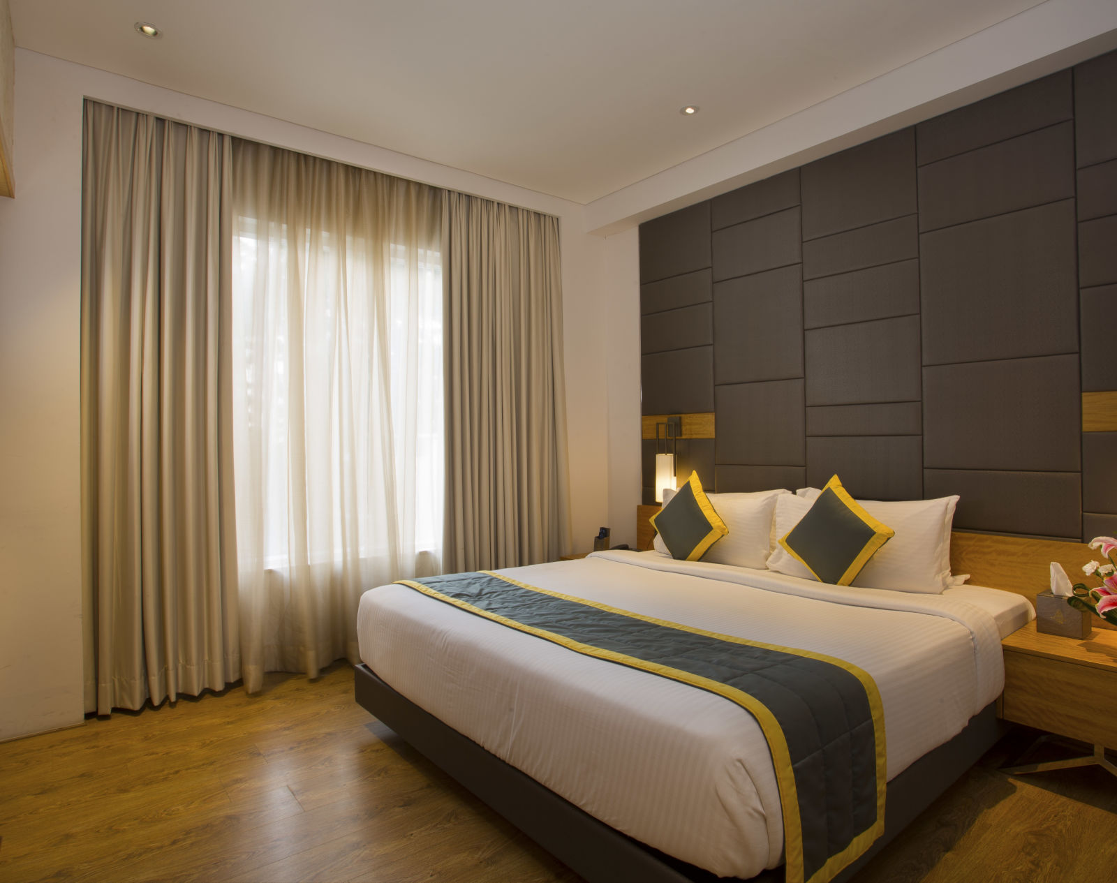 a bedroom with a large bed opposite a television mounted on the wall and side drawers on each side - Hotel Fountain Tree By TGI - JP Nagar, Bangalore