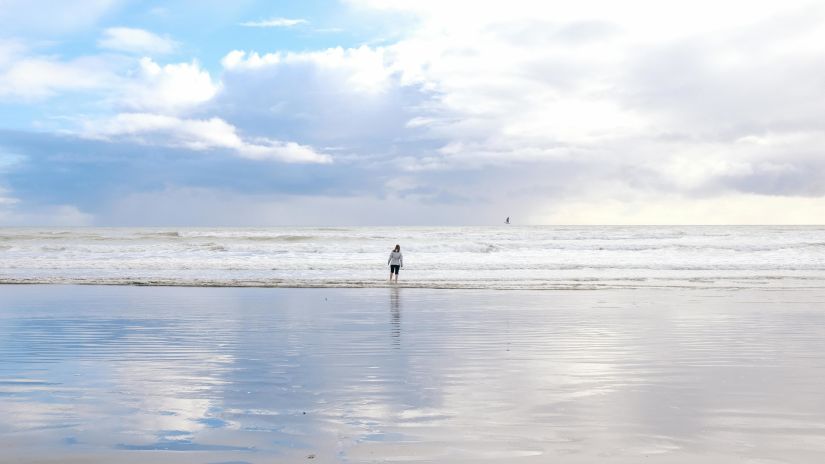 A person walking towards the ocean at a beach on a cloudy day