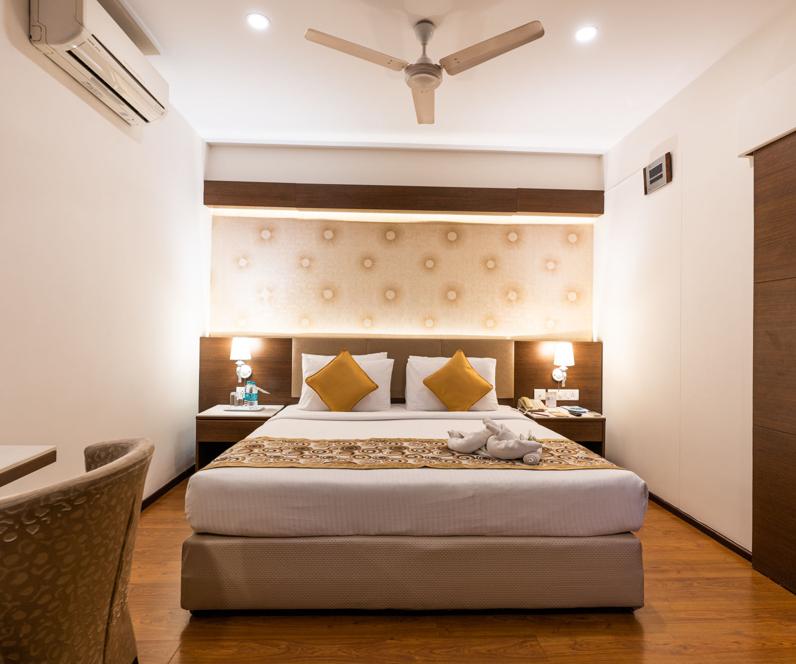 a double bed with a fan hung above it and an AC next to it inside one of the rooms - Hotel Pai Vista, Mysore