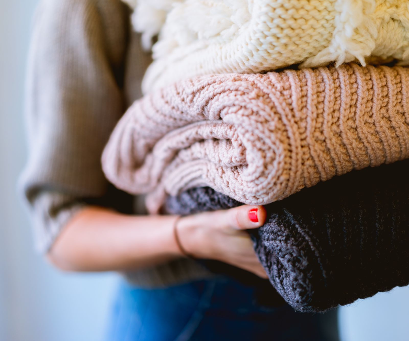 Person holding a stack of folded knitted blankets in neutral colors.