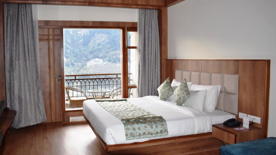 The bedroom with a double cot bed and a door leading to the balcony at The Orchid Hotel, Manali