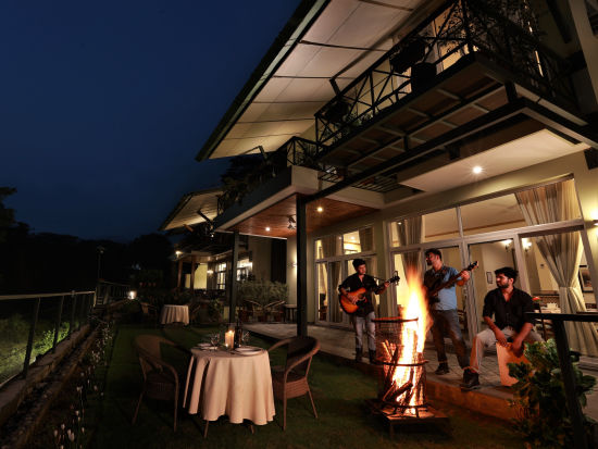 A bonfire with two people playing guitars under the night sky in front of villas at Lamrin Norwood Green, Palampur