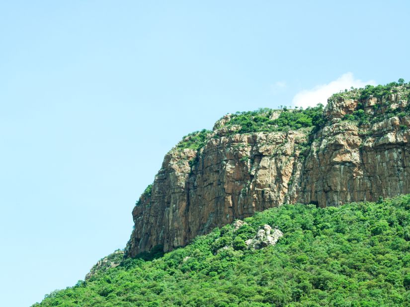 an open mountain with greenery below and above it and blue sky in the background