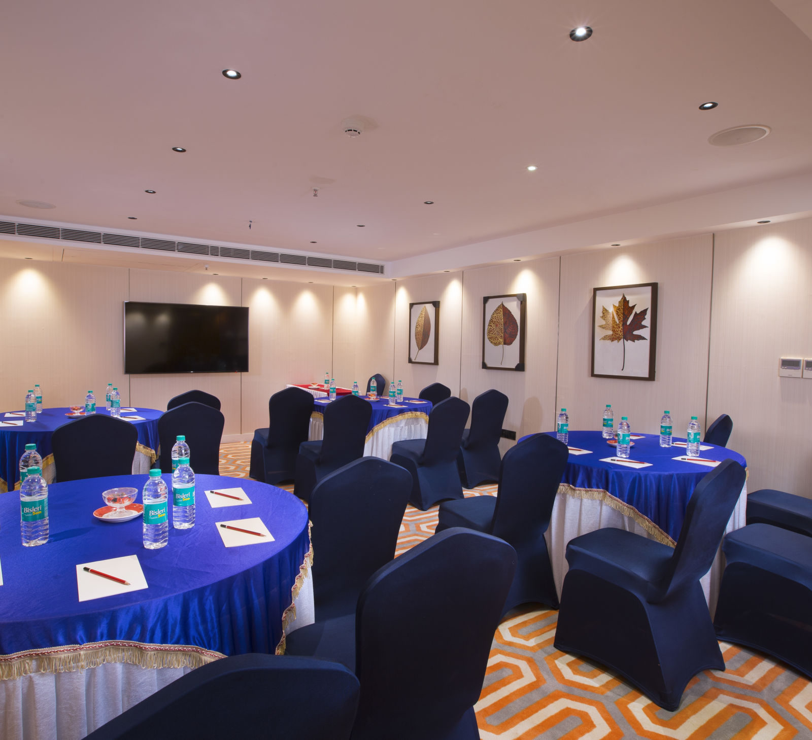 An intimate boardroom setting with round tables covered in blue cloth, blue chairs and a large flat-screen TV - Hotel Southend by TGI - Bommasandra, Bangalore