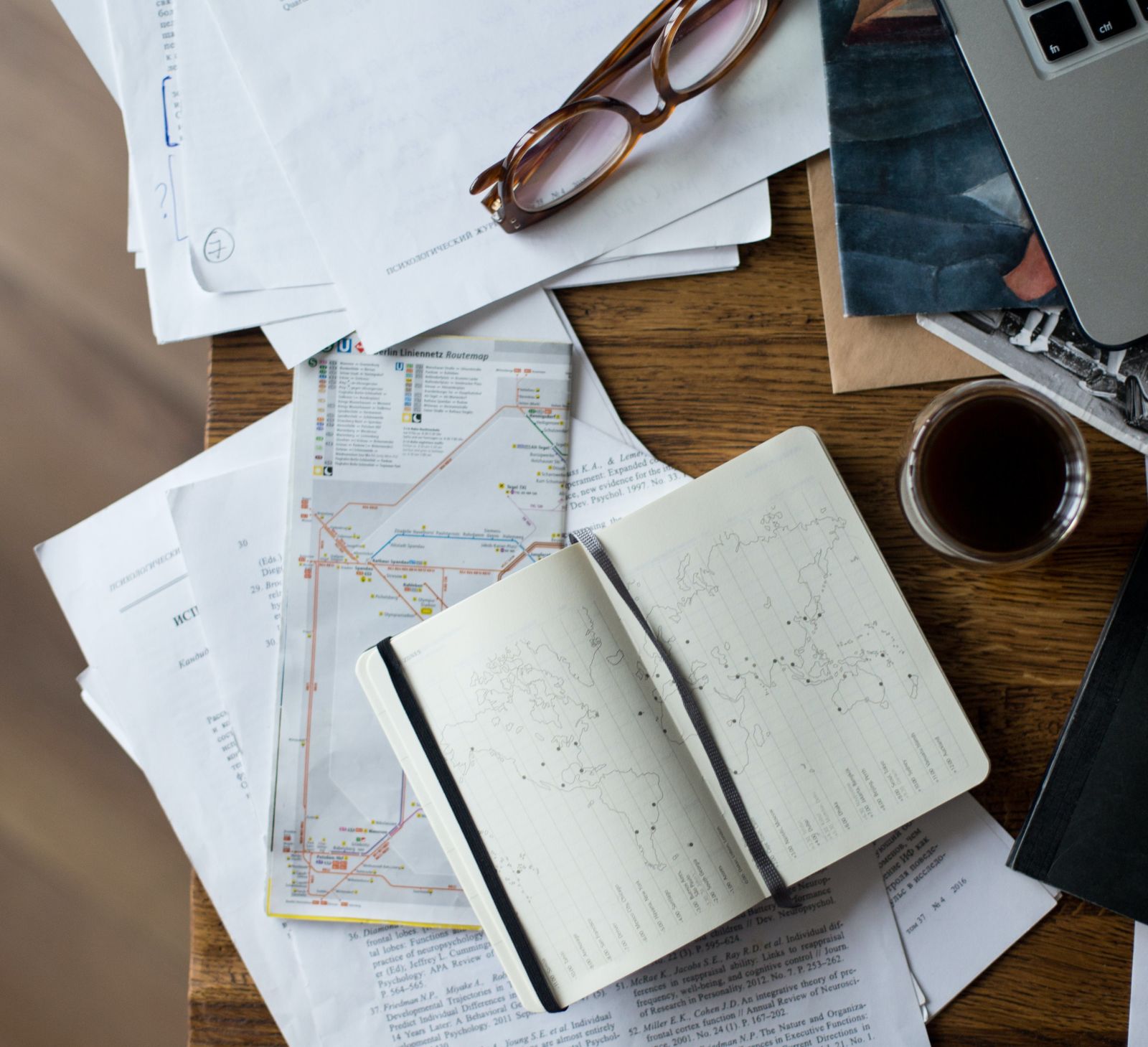 A wooden desk with a journal, coffee, pen and laptop