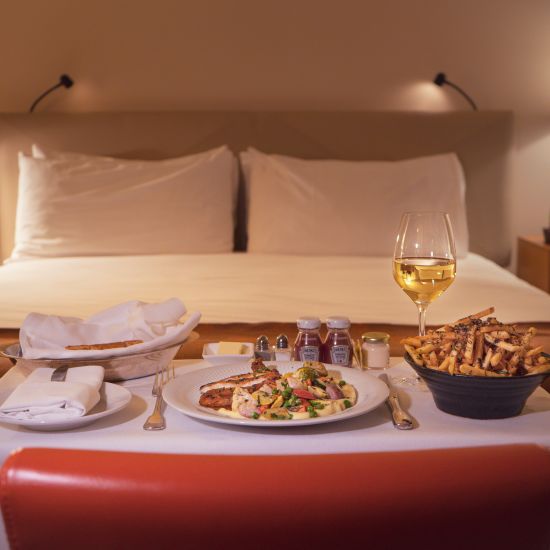 Many items on a table that was served as room service with a double bed in the background