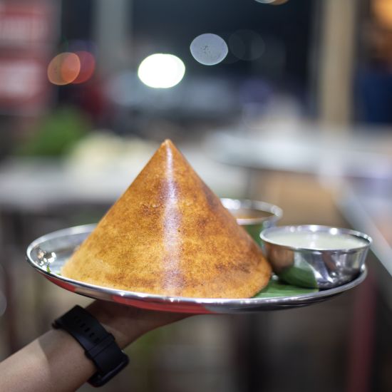 A POV shot of a person holding conical dosa sided with chutney on a plate 