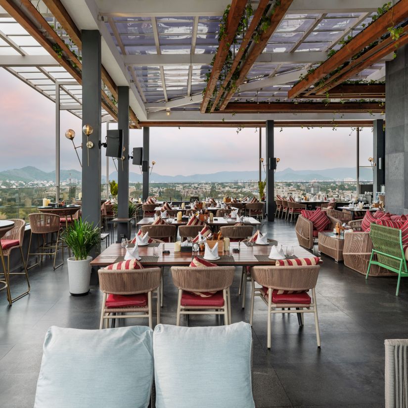 A beautifully decorated seating arrangement inside Taro, providing an open view of Udaipur's magnificent scenic beauty, at Parallel Hotel Udaipur