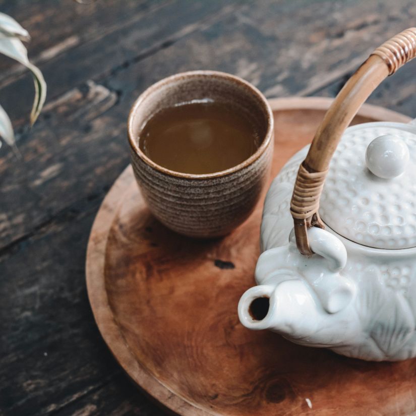 a tray with a pot and a clay cup filled with tea and a potted plant next to it