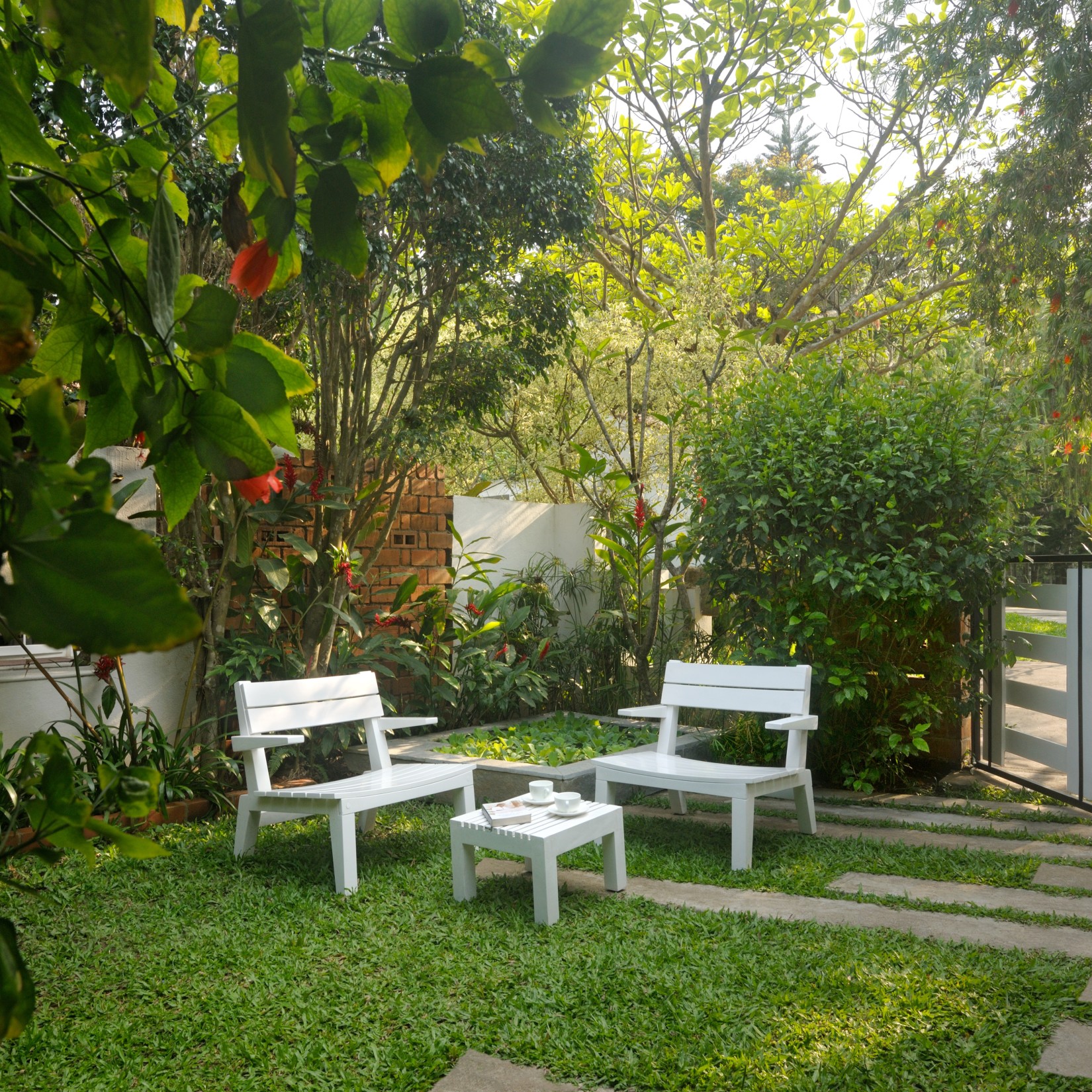 White outdoor seating arrangement in a garden with lush plants and a walking path