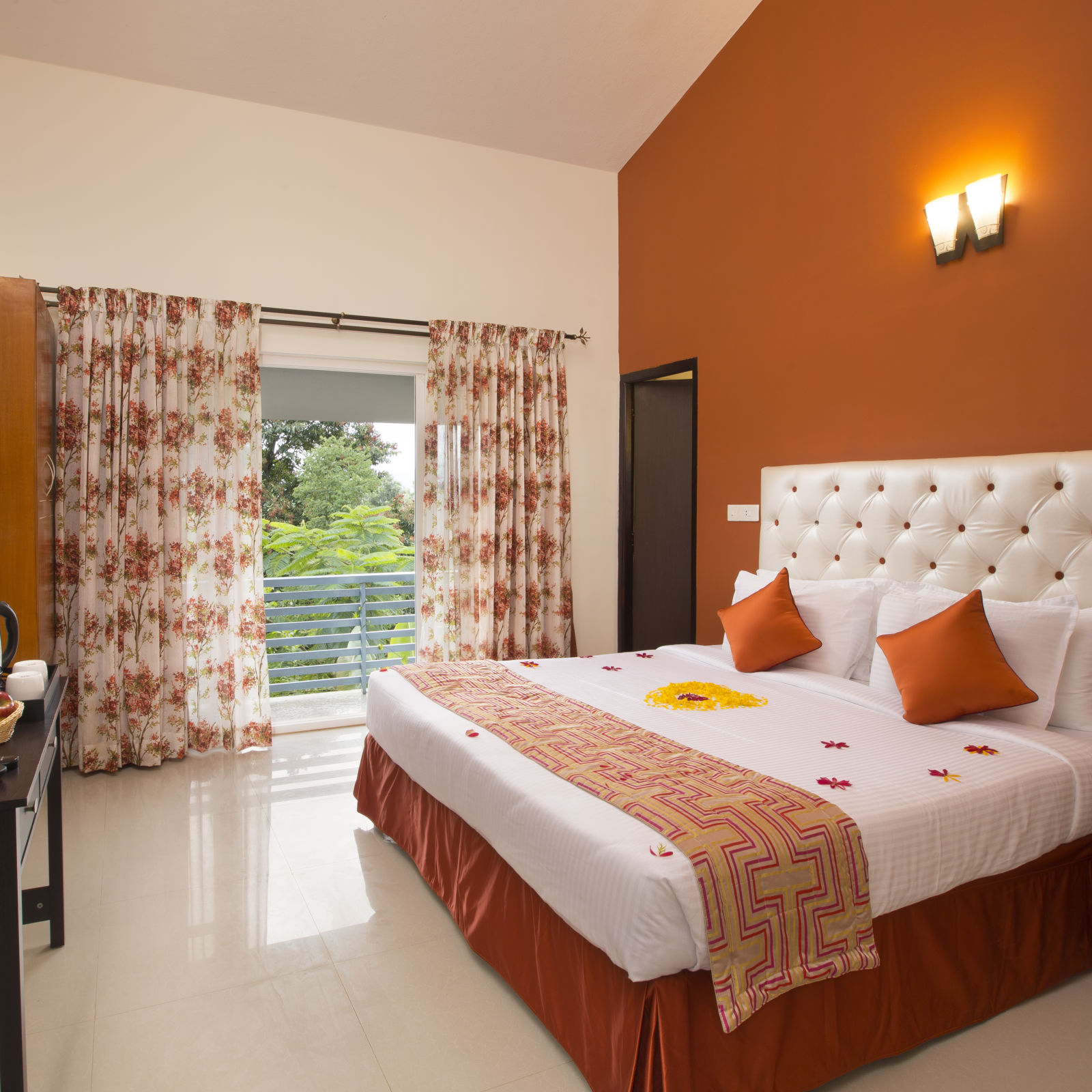 A bright and inviting hotel room with a white tufted headboard, orange accents and floral curtains with a view  - Kairos, Yelagiri