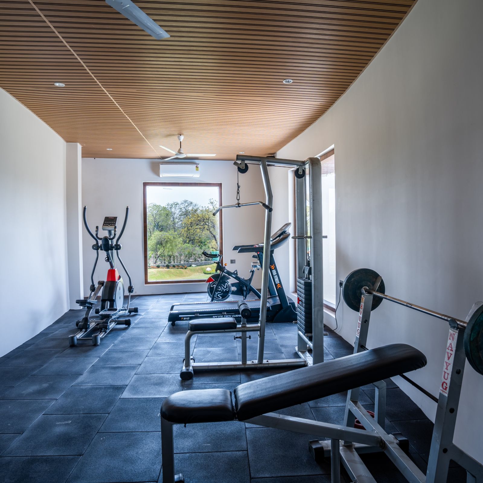 A gym room with cycling machines, a bench press, a thread mill and a lat pull down machine - Shervani Pebbles & Pines, Corbett