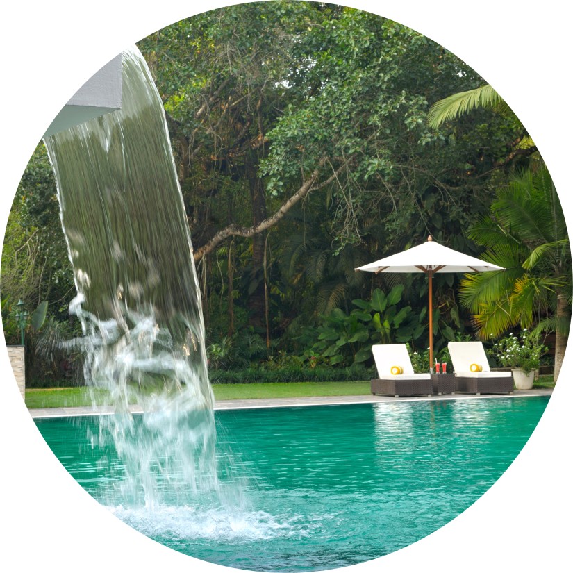 Swimming pool with a waterfall feature surrounded by lush greenery.