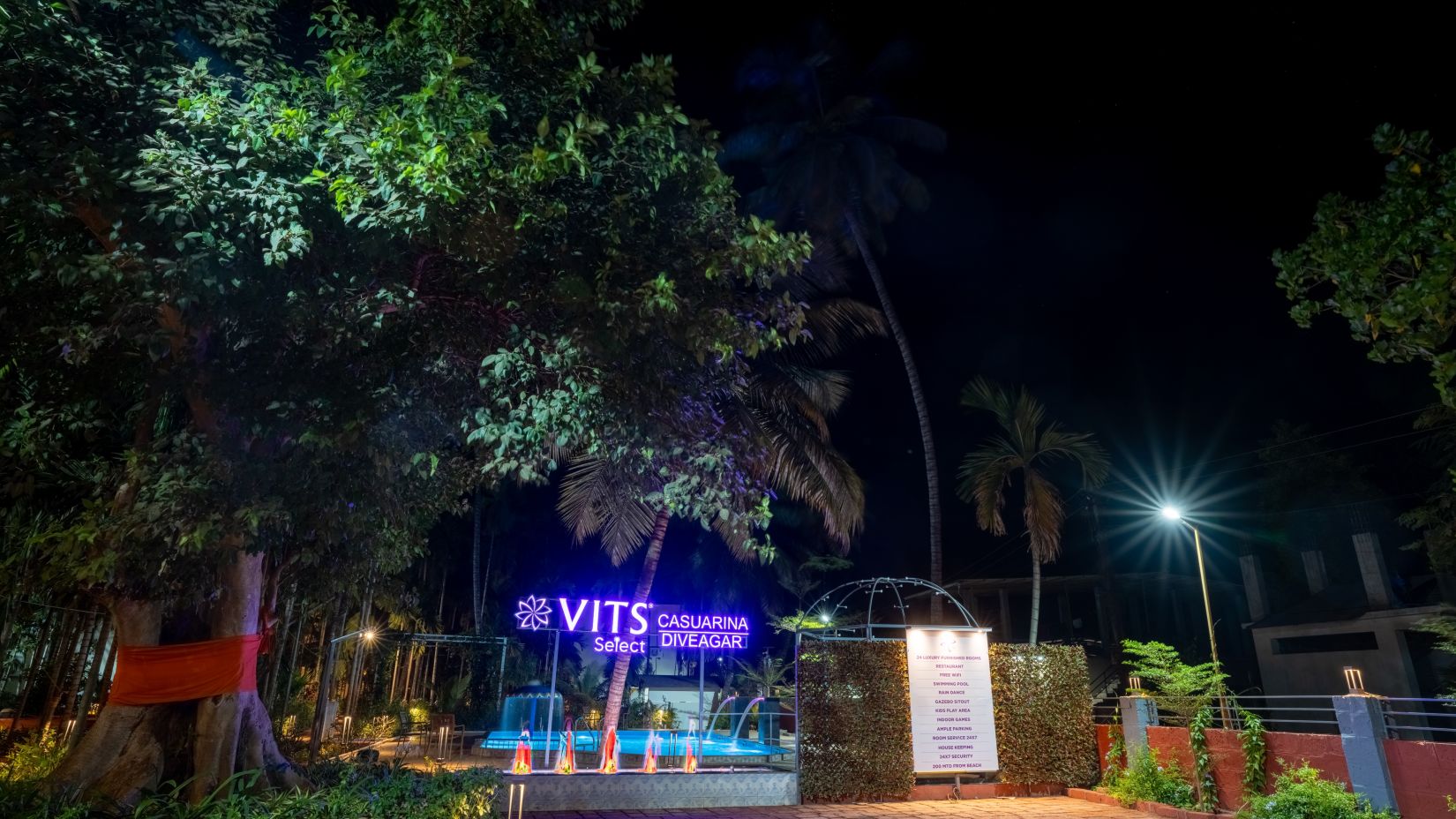 Signage of VITS Select Casuarina Diveagar in neon colours in the night with a large tree next to it