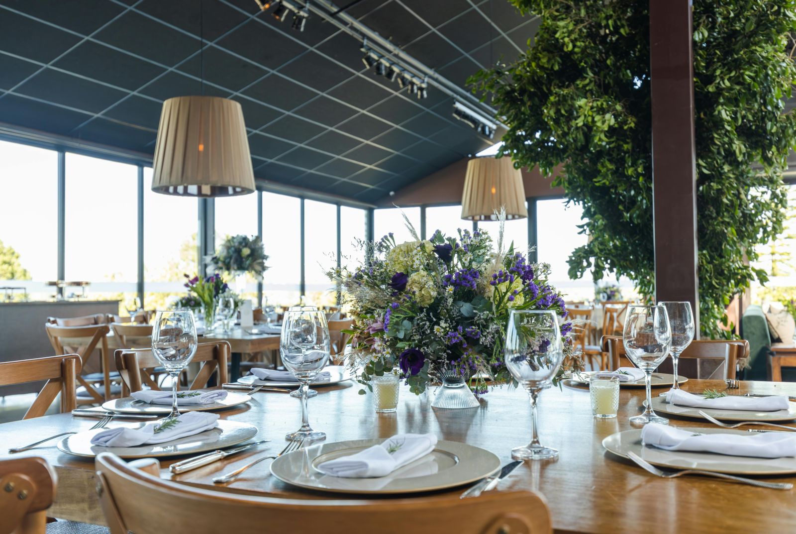 A well-appointed restaurant setting with tables set with fine china and glassware, surrounded by natural light and greenery.