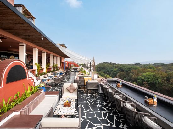 A rooftop terrace with chic outdoor furniture, a striking black and white floor, and lush greenery in the background.