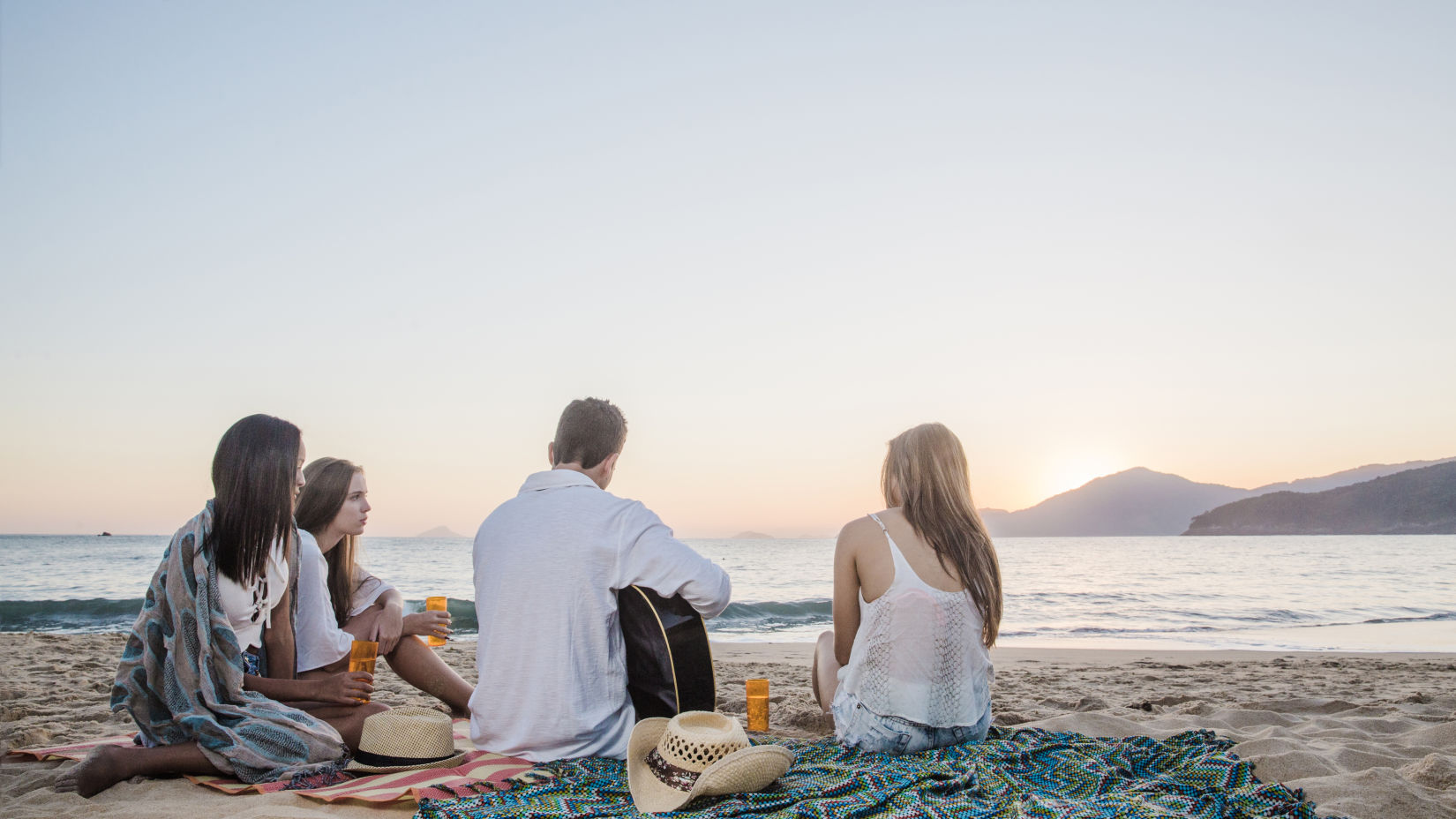 a group of 4 friends captured during the day sitting by the beach after a picnic