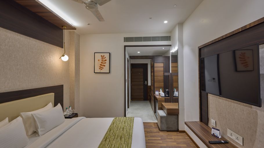 A king bed with a tv wall mounted opposite it inside the deluxe room at Grand Continent - A Sarovar Premiere Affiliate Hotel, Hosur