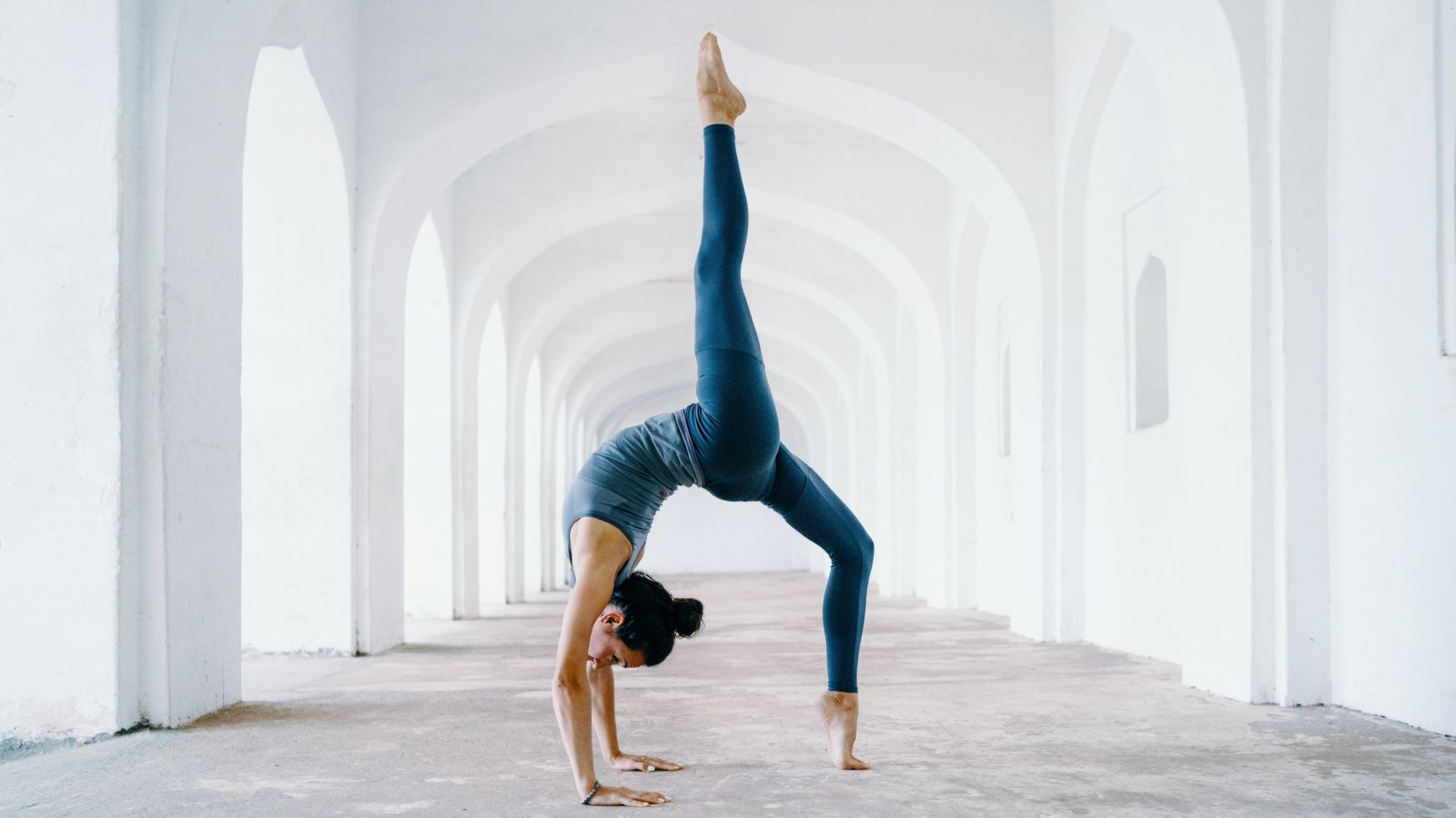 a woman performing a yoga pose in a corridor of a white building