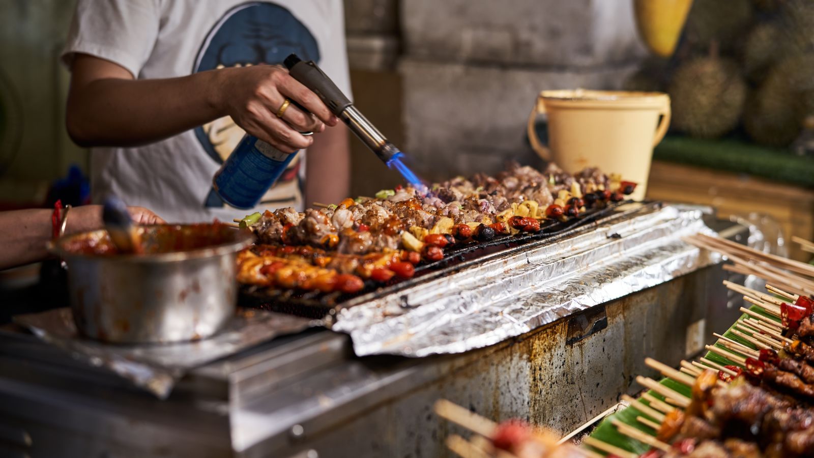 A street food vendor frying meat that is lined up in skewers