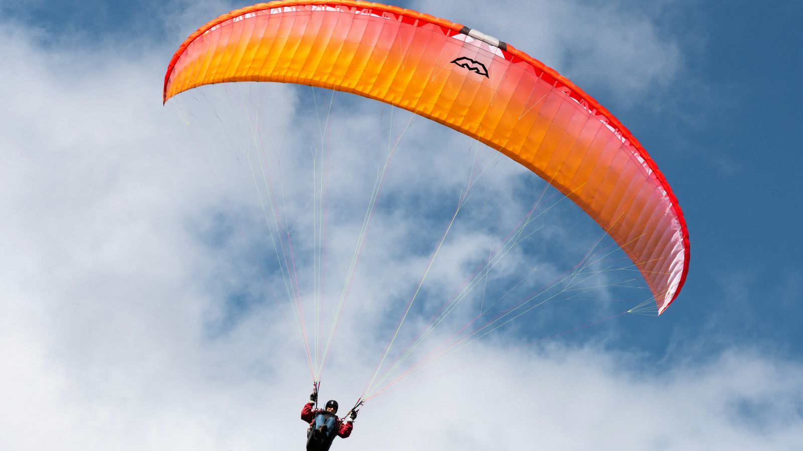 a person paragliding with a an orange parachute and blue sky in the background