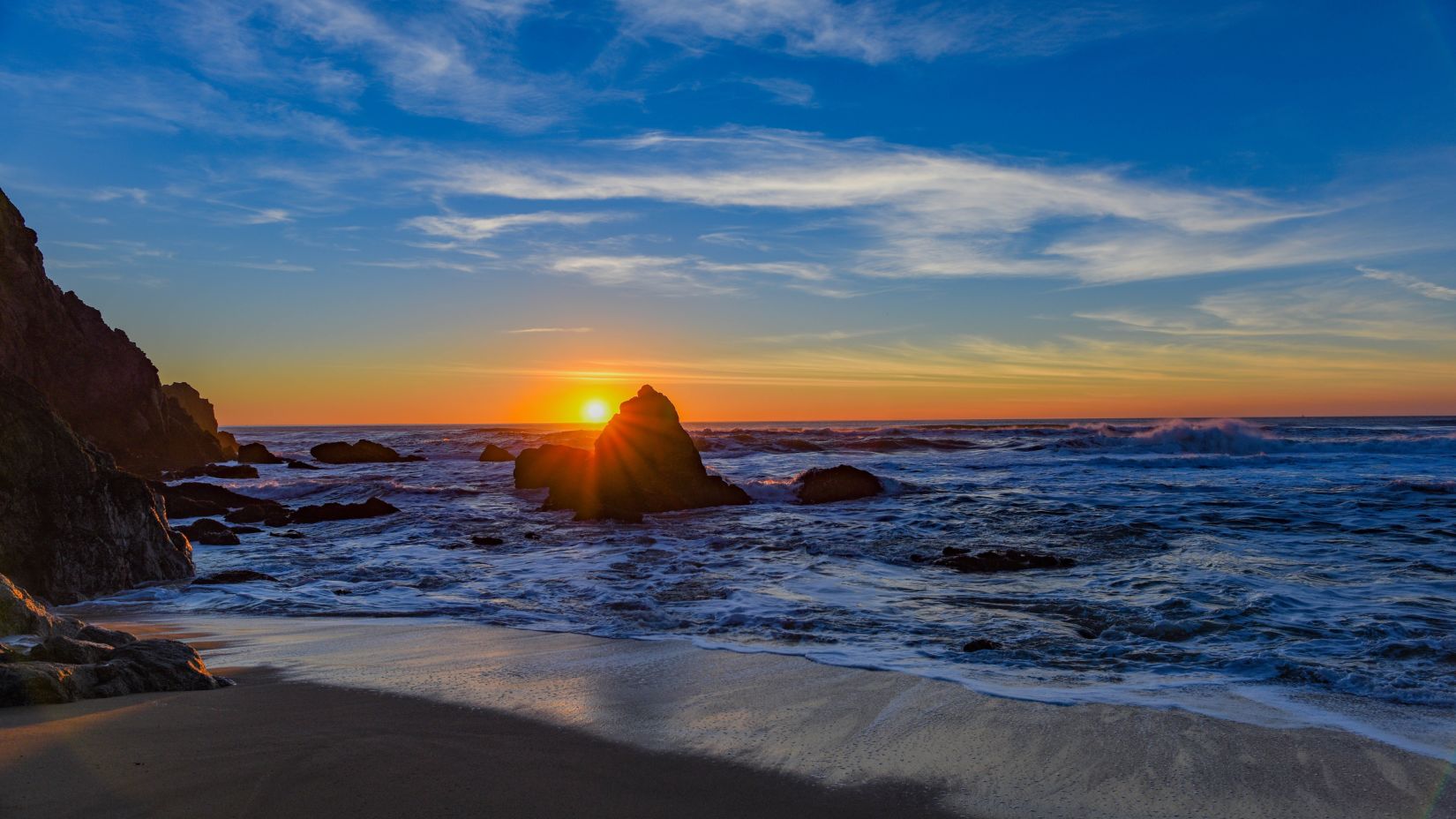 sun setting behind a rock near a beach