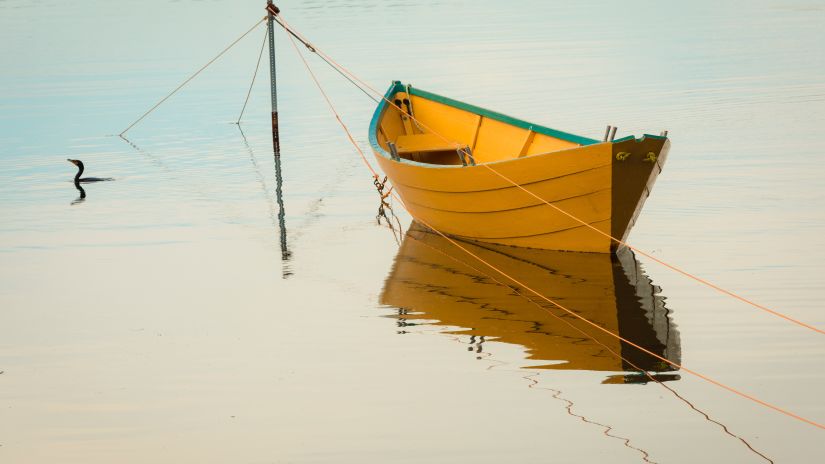 A solitary boat parked in a water body with the reflection of the sky showing on the water body