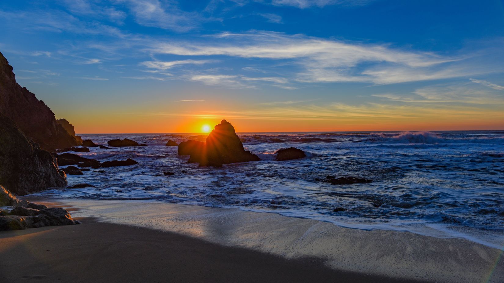 sun setting behind a rock near a beach