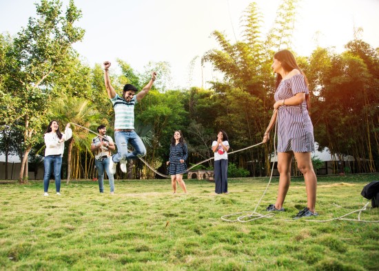 alt-text A group of adults and children playing tug of war in a grassy outdoor area, displaying joy and family bonding during a playful and competitive moment.