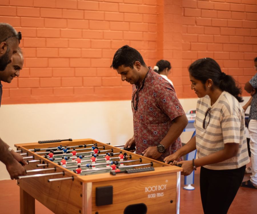 alt-text a group of people playing foosball inside the game room at Ibex River Resort, Pollachi