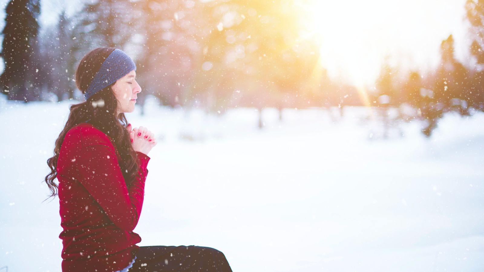 a woman praying on top of a snow covered mountain with the sun setting in the background