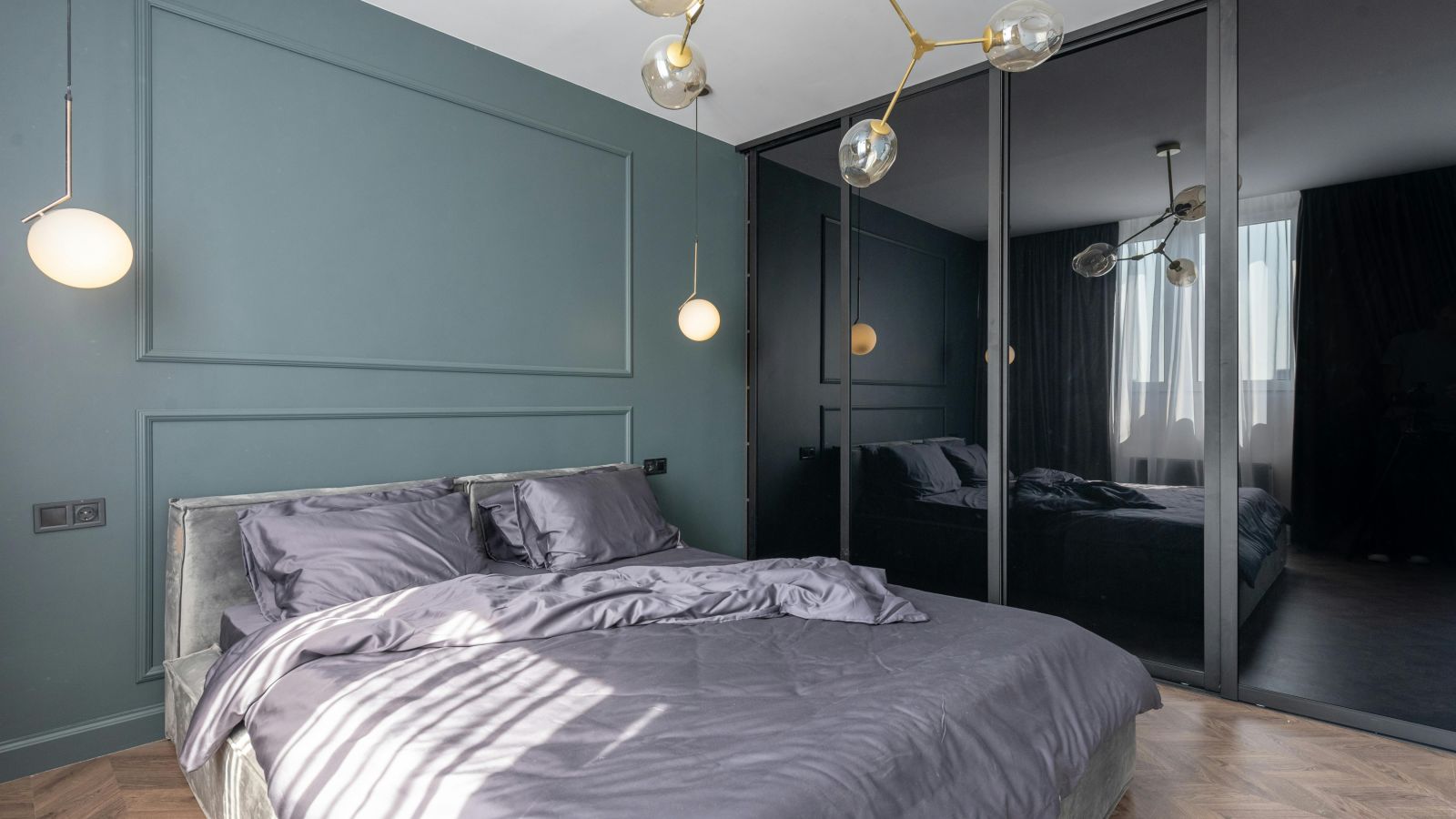 image of a modern bedroom with teal coloured master wall featuring a plush bedding in the middle with black panel wardrobein the corner of the room