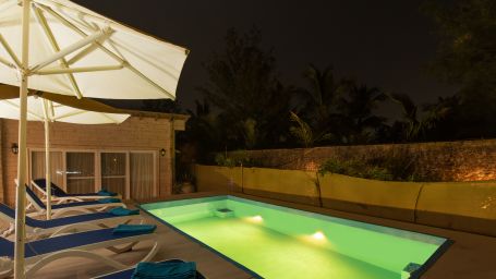 Swimming poolside view at night with pool loungers umbrellas and lightings
