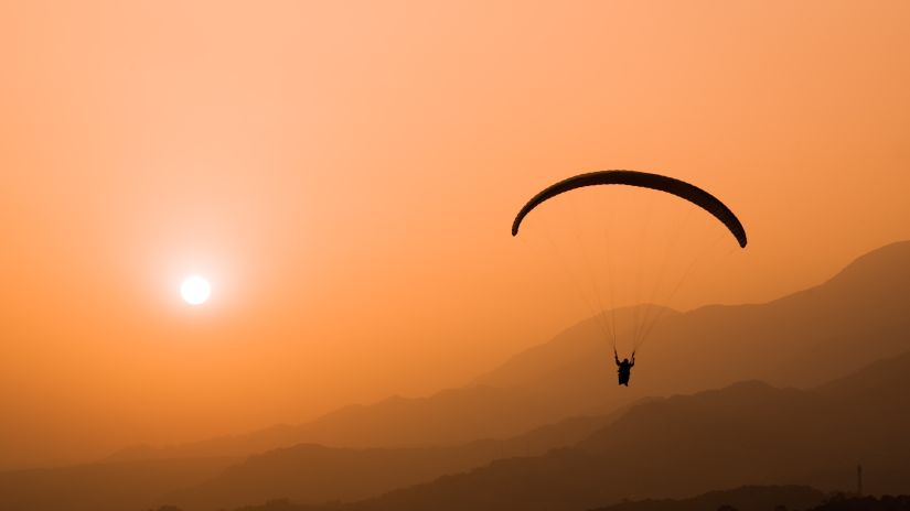 an image of a person paragliding during sunset in a place surrounded by mountains and trees  @ @ Lamrin Norwood Green, Palampur